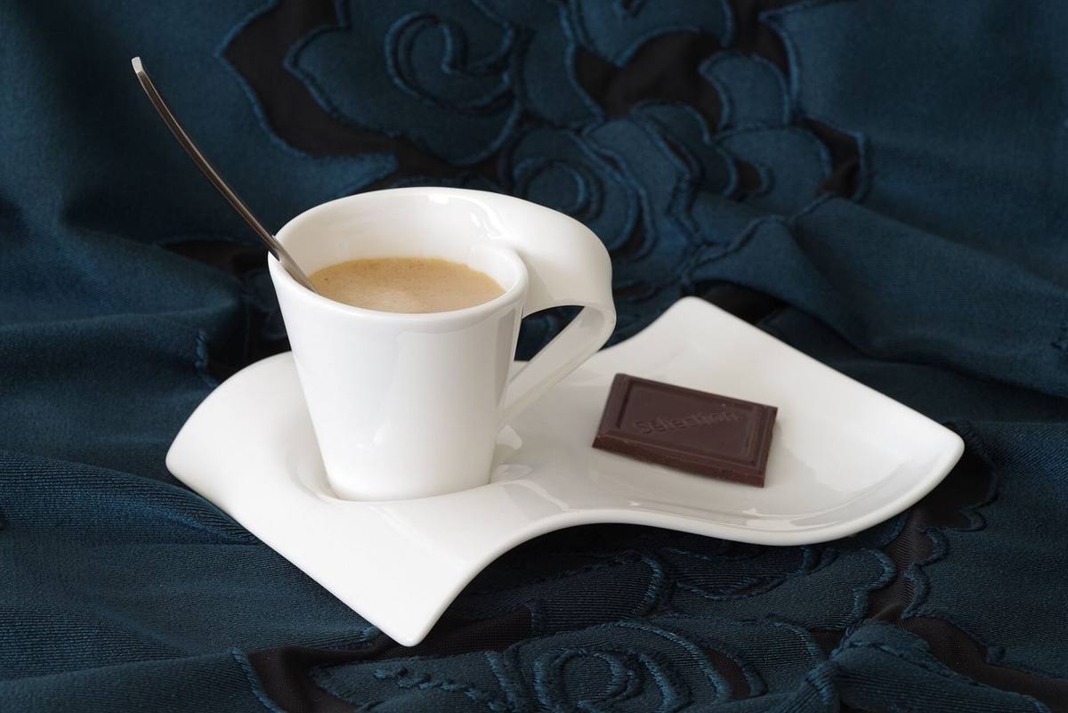 A white espresso cup on a saucer with a square of chocolate